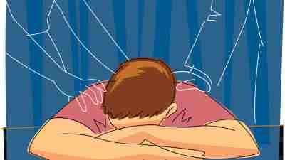 A depressed male Caucasian teen with his head in his folded arms and outlines of his parents hands on his back