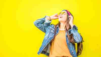Smiling Woman Looking Upright Standing Against Yellow Wall