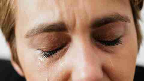 A closeup of a woman with closed eyes, a tear streaming down her face.